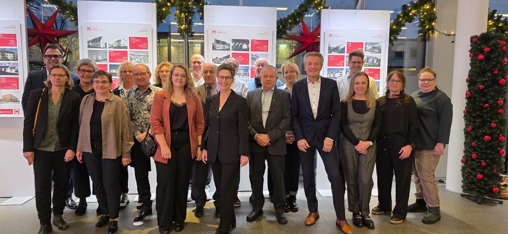 Gruppe von Menschen in Geschäftskleidung steht vor mehreren beleuchteten Informationswänden in einem festlich geschmückten Raum